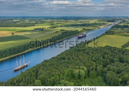 Aerial view of Kiel Canal with container ship and  traditional sailing vessel.Container cargo ship and tall ship on the Kiel Canal between Baltic sea and North Sea Schleswig Holstein, Germany. Royalty-Free Stock Photo #2044165460