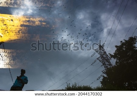 Blurred silhouette of reflection of one person walking alone on wet city sidewalk on rainy day. Birds are flying across the sky. Abstract photography.