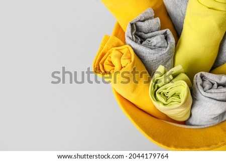Hat with rolled clean clothes on grey background, top view