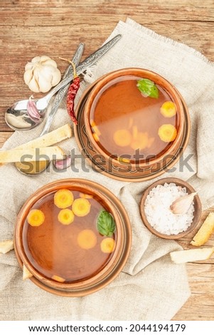 Transparent chicken broth with vegetables in ceramic bowls. Traditional bouillon, healthy food, cutlery. Old wooden background, top view