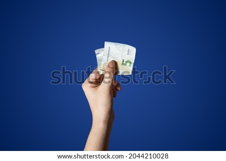  Hand holding a 5 Euro bill isolated on blue background. High quality photo
