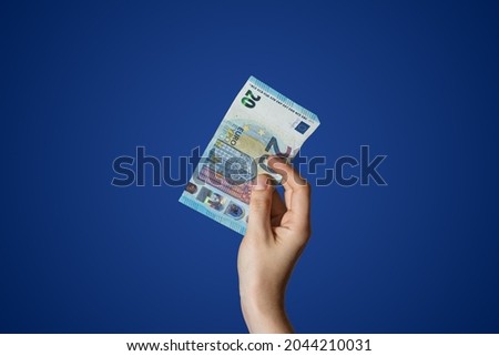  Hand holding a 20 Euro bill isolated on blue background. High quality photo Royalty-Free Stock Photo #2044210031