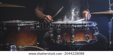 A male drummer plays snare drum with drumsticks in a dark room.
