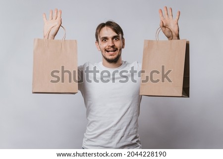 A young man in a white T-shirt holds clean paper bags in his hands. Handsome guy with purchases in his hands on a white background. Mock-up.