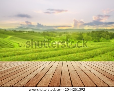 empty wooden desk with blurry tea plantation on hill against evening sky and leave as frame Product display stand natural background concept