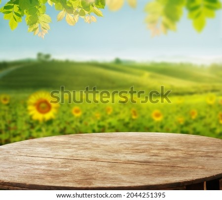 empty wooden desk with blurry Sunflower field against tea plantation on hill and leave as frame Product display stand