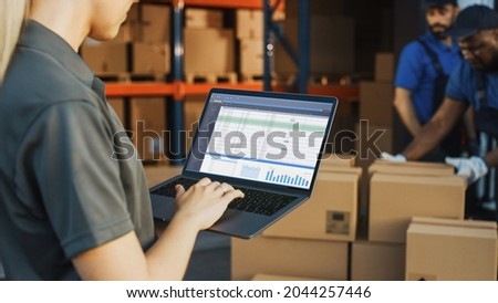 Female Manager Using Laptop Computer To Check Inventory. In the Background Warehouse Retail Center with Cardboard boxes, e-Commerce Online Orders, Food, Medicine, Products Supply. Over the Shoulder Royalty-Free Stock Photo #2044257446