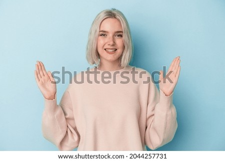 Young caucasian woman isolated on blue background holding something little with forefingers, smiling and confident.