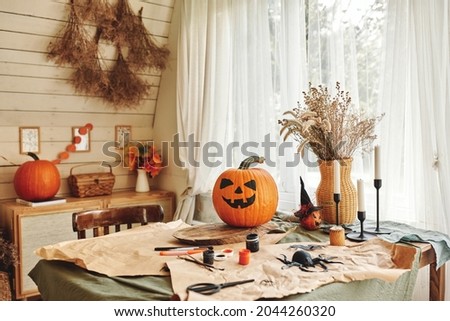 Happy Halloween. Carved orange pumpkin with drawn spooky face standing on wooden table in cozy rustic kitchen, classic Jack-o-lantern in house interior during holiday preparation