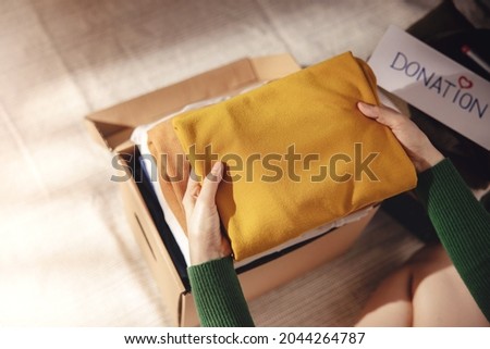 Clothes Donation Concept. Box of Cloth with Donate label. Woman Preparing Used Old Garment at Home. Top View Royalty-Free Stock Photo #2044264787