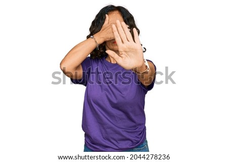 Middle age hispanic woman wearing casual clothes covering eyes with hands and doing stop gesture with sad and fear expression. embarrassed and negative concept. 