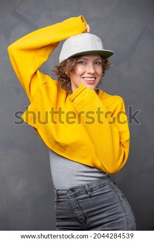  Autumn mood! Portrait of happy smiling woman with short brunette curly hair wearing yellow sweater and a hat over grey wall background