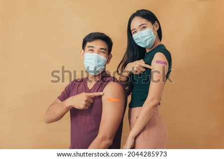 Asian man and woman showing shoulders after getting a vaccine. Happy couple showing arm with band-aids on after vaccine injection. Royalty-Free Stock Photo #2044285973
