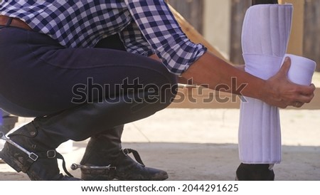 an unknown person with spurs on his boots bandages a horse . High-quality photo