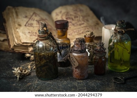 Magic potions in bottles, ancient books and witchery herbs on wooden background, Halloween theme Royalty-Free Stock Photo #2044294379