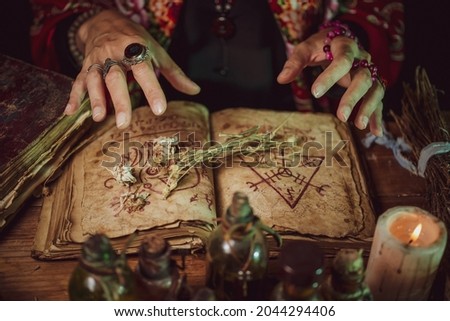Female witch making potion on dark background, magic bottles with potions and candles on table of alchemist, Halloween theme Royalty-Free Stock Photo #2044294406