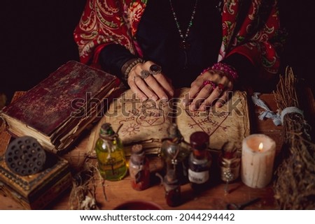 Female witch making potion on dark background, magic bottles with potions and candles on table of alchemist, Halloween theme Royalty-Free Stock Photo #2044294442