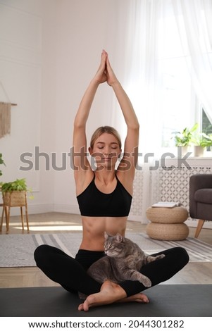 Beautiful woman with cat practicing yoga at home
