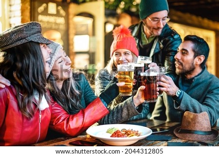 Happy multicultural friends drinking beer with nachos outdoors at night - Food and beverage lifestyle concept on young people enjoying time together outside - Warm filter with focus on glasses