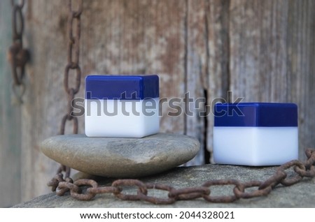 two jars cosmetic for cream with a place to record the logo on a stone with a wooden background and a large metal chain