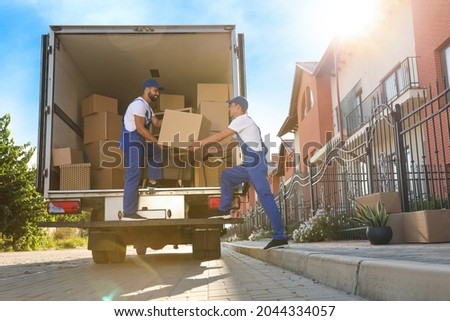 Workers unloading boxes from van outdoors. Moving service Royalty-Free Stock Photo #2044334057