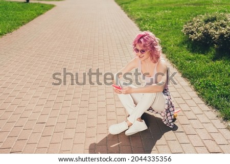 Portrait of attractive cheerful girl sitting on skate using device gadget chatting on fresh air traveling outdoors