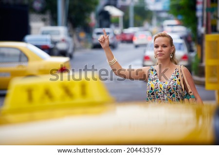 blond businesswoman calling yellow taxi with arm raised in street. Tourism and business travel 