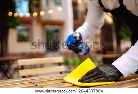 Disinfecting to prevent COVID-19. Waiter cleaning the table with Disinfectant Spray in a restaurant wearing protective medical mask and gloves.