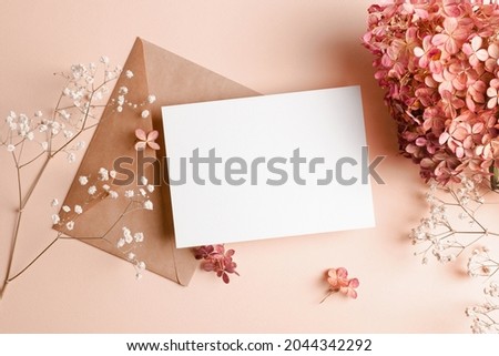 Invitation or greeting card mockup with envelope, hydrangea and gypsophila flowers. Blank card mockup on pink background.