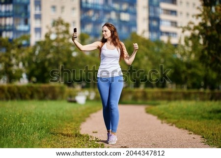 Young white woman takes pictures of herself jogging using smartphone.