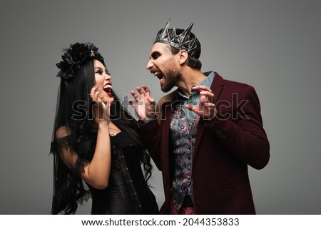 spooky interracial couple in vampires halloween costumes frightening each other isolated on grey