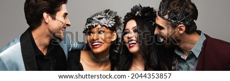 joyful interracial friends smiling at each other during halloween party isolated on grey, banner