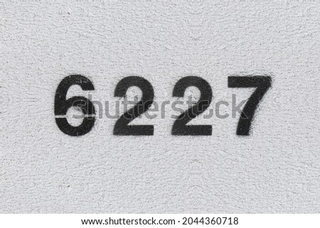 Black Number 6227 on the white wall. Spray paint. Number six thousand two hundred and twenty seven.