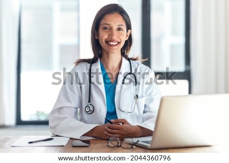 Shot of attractive female doctor smiling looking at camera while working with laptop in the consultation. Royalty-Free Stock Photo #2044360796
