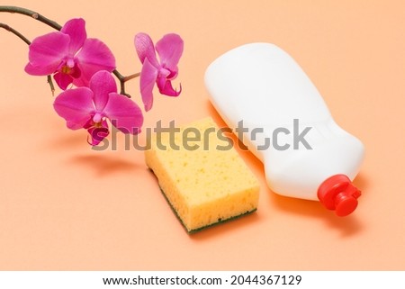 Plastic bottle of dishwashing liquid, a sponge and orchid flowers on a beige background. Top view. Washing and cleaning set.