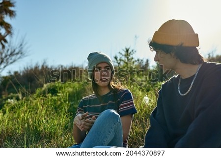 Two intrigued young people sitting on a hill and looking at each other in deep thought