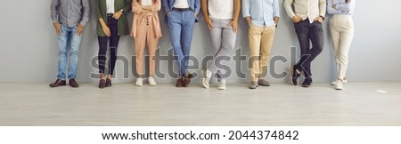 Group of successful confident business people in smart and casual wear standing in studio. Team of employees leaning on grey office wall. Cropped shot of people's legs in classic pants and jeans Royalty-Free Stock Photo #2044374842