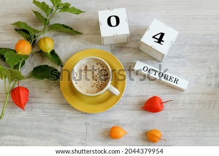 Calendar for October 4 : the name of the month in English, cubes with the numbers 0 and 4, a yellow cup with hot coffee, branches of physalis with orange boxes on a gray background
