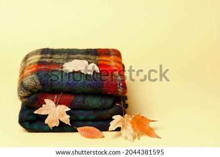 autumn woolen check scarf on a yellow background with yellow autumn leaves