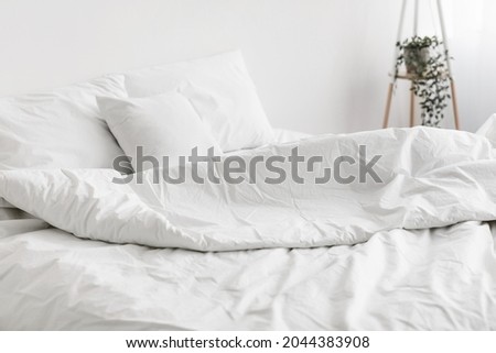Soft unmade bed, comfortable pillow, white linen with nobody. Bedding, duvet, modern apartments and domestic cozy, free space. Good morning and modern bedroom interior, room design in day light Royalty-Free Stock Photo #2044383908