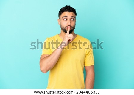 Young arab man isolated on blue background showing a sign of silence gesture putting finger in mouth