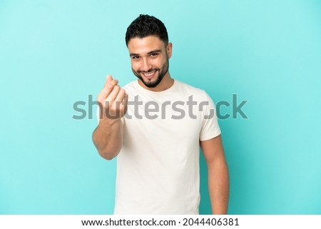 Young arab man isolated on blue background making money gesture