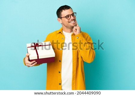 Brazilian man holding a gift over isolated blue background thinking an idea while looking up