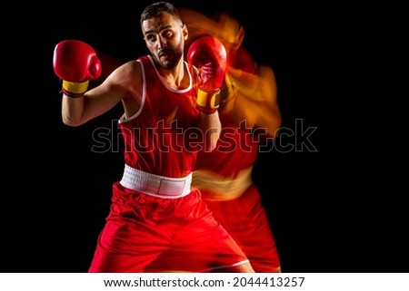 Ready to knock down the opponent. Heavy punch move. One professional male boxer training isolated over black backgrund in mixed light. Concept of health, sport, motion, strength. Copy space for ad.