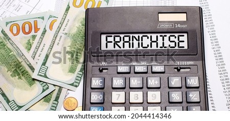 Against the background of cash and documents is a black calculator with the text FRANCHISE on the scoreboard. Business concept