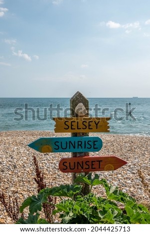 fun sign on the beach at Selsey West Sussex England pointing to the sunrise and sunset	