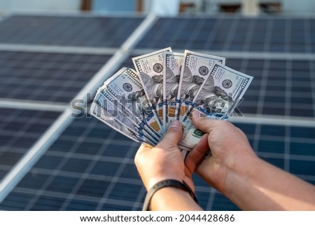 male hand hold hundred dollar at the background of solar station.  concept of generation 