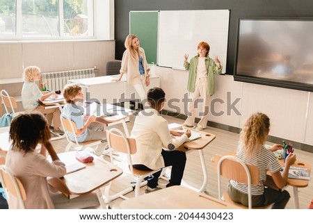 Schoolgirl pupil student answering at the blackboard, presenting project homework during class lesson at school. Teacher listening to student`s answer Royalty-Free Stock Photo #2044430423