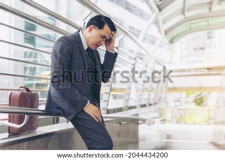 business man wearing a suit is stressed from work stopped on a public walkway , He had a serious ,worried face because he was fired from his job the company he works for is about to go bankrupt Royalty-Free Stock Photo #2044434200