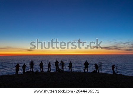 unfocused dark silhouettes of tourists photographers take pictures of the morning sunrise over the clouds, travel or vacation concept, selective focus